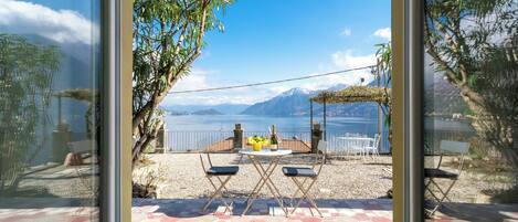 A patio with a table and chairs, a bottle of wine, and a view of a lake and mountains.
