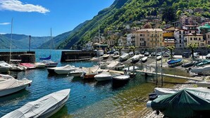 Una marina con barcos amarrados, rodeada por un pueblo en la ladera de una colina, con edificios y una montaña al fondo.
