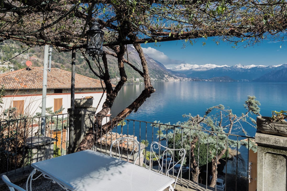A terrace with a table and chairs overlooking a lake with mountains in the background.