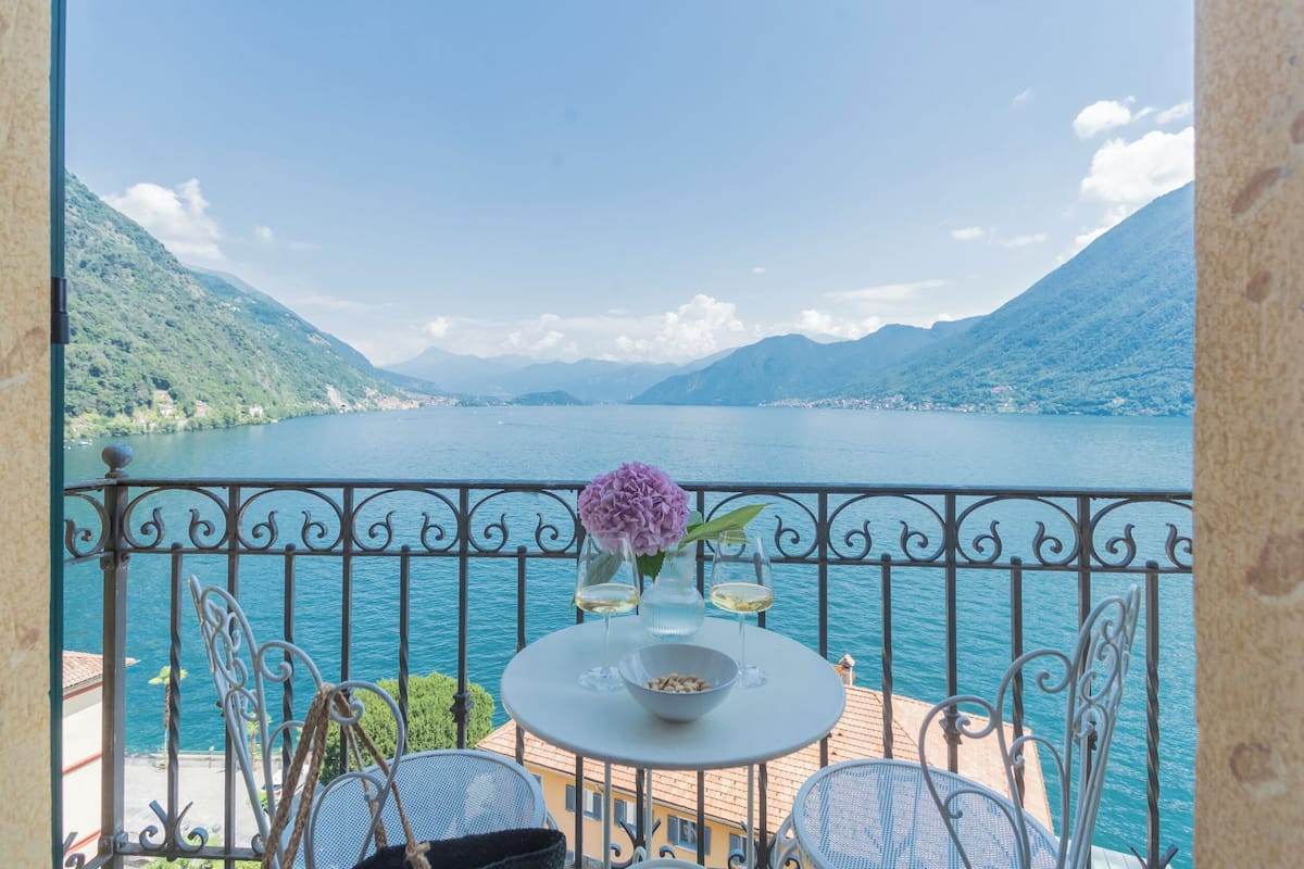 A balcony with a table set for two, overlooking a lake with mountains in the background.