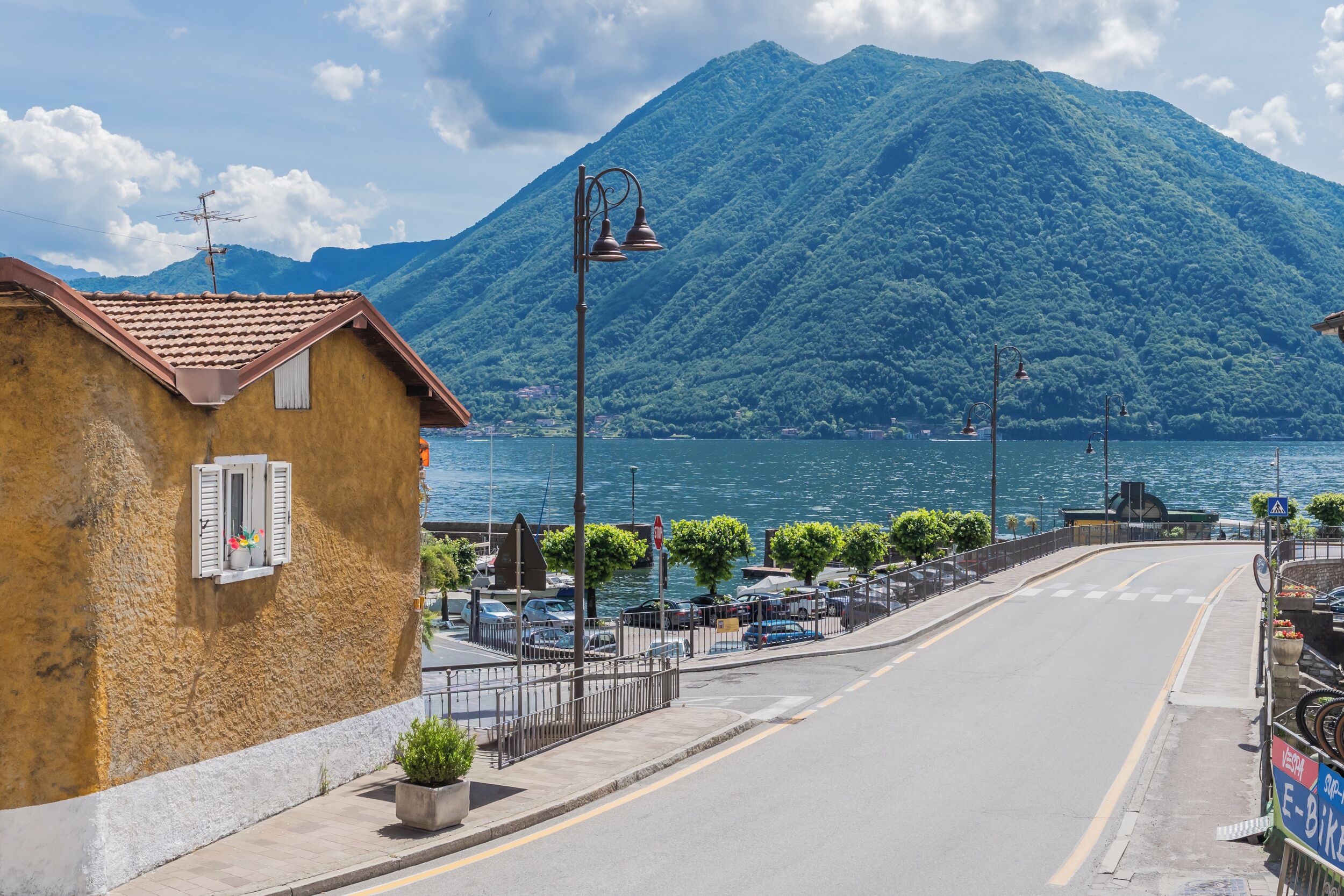 A coastal street with a mountain backdrop, a yellow building with shutters, and a clear sky.