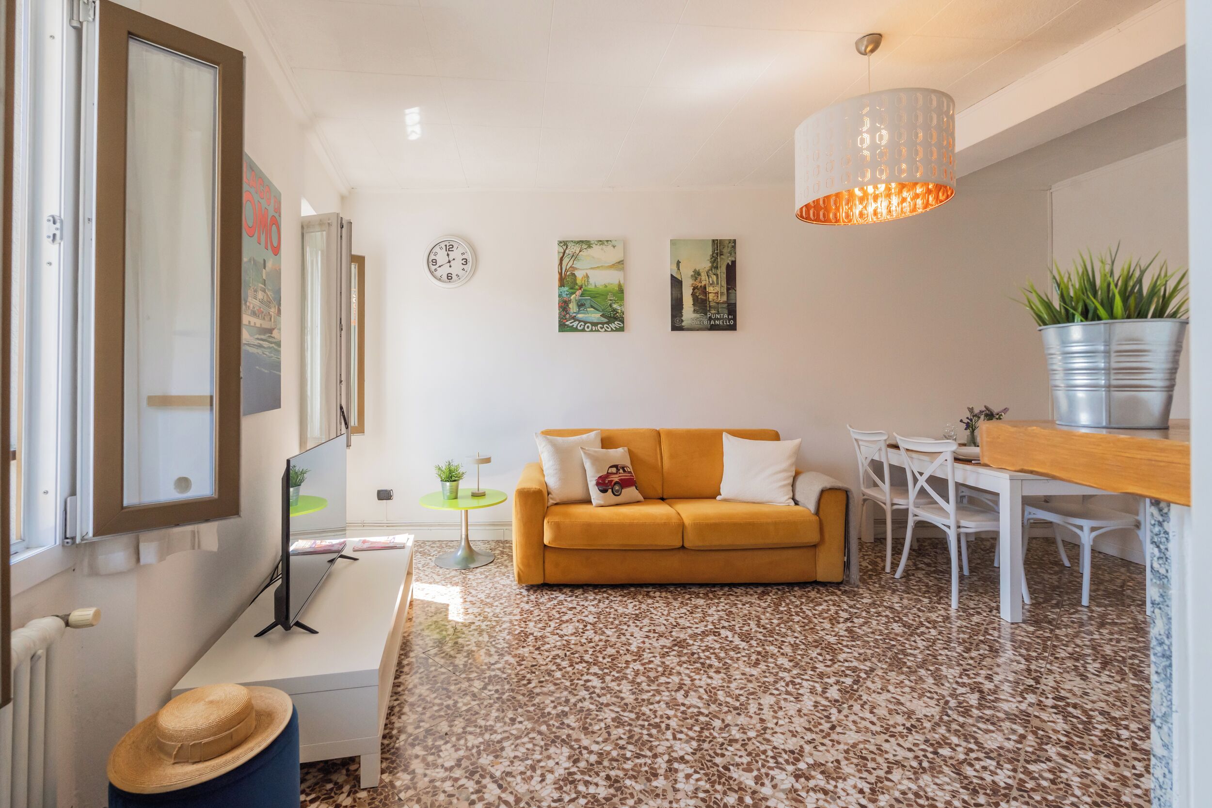 A living room with a sofa, a coffee table, a dining table with chairs, a potted plant, and a wall clock.