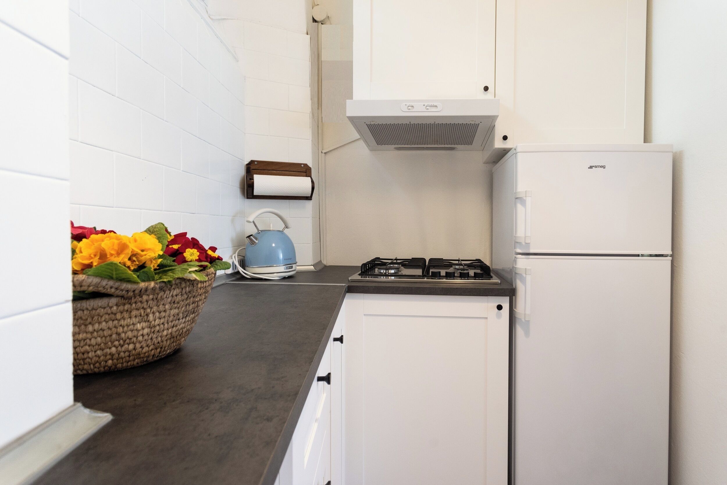 A kitchen with white cabinets, a gas stove, a white refrigerator, and a blue kettle.