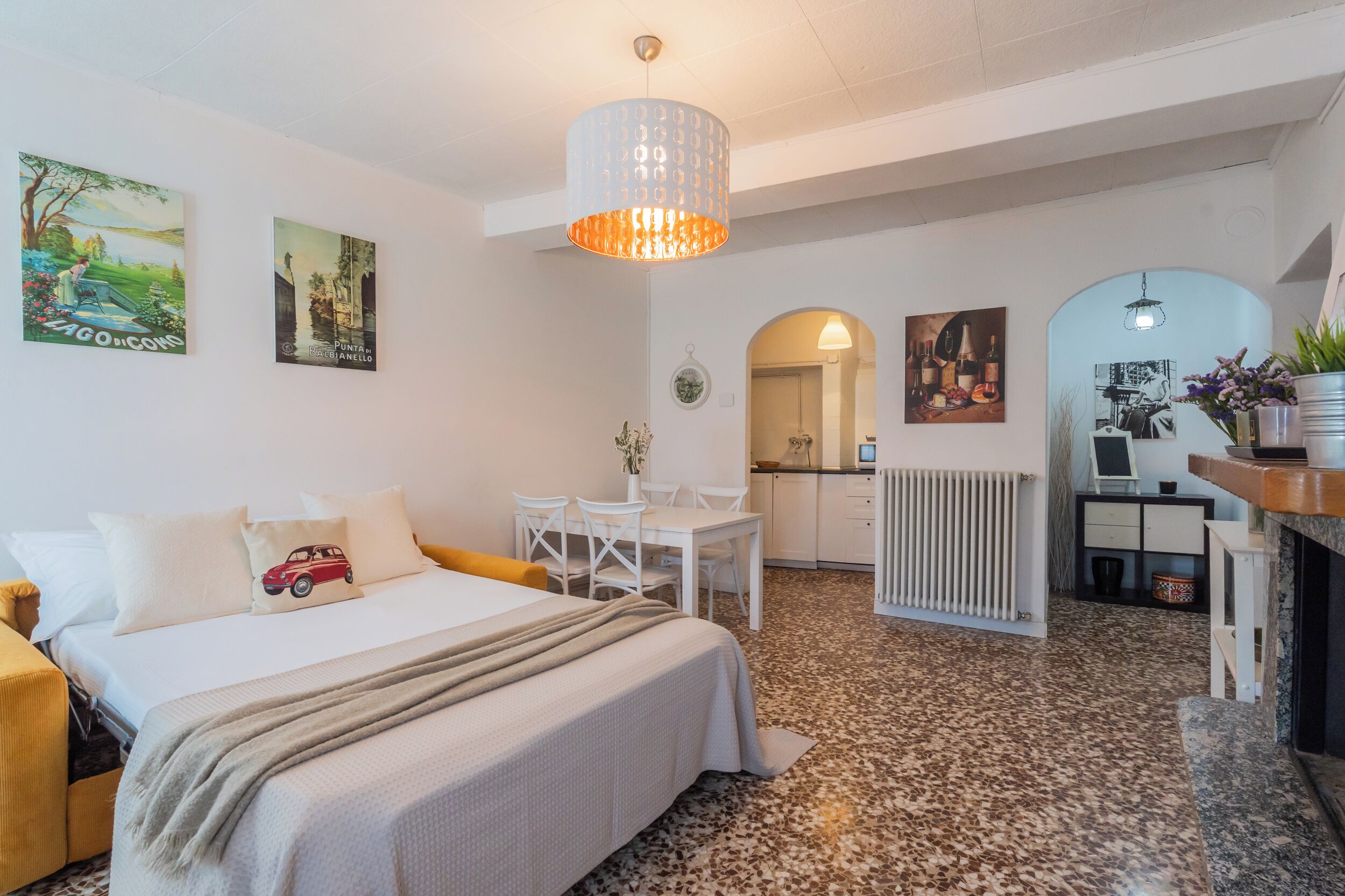 A hotel room with a bed, a desk, a chair, a radiator, and artwork on the walls.