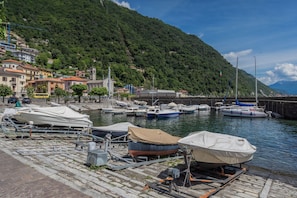 Un puerto deportivo con barcos amarrados, un paisaje montañoso al fondo y edificios a lo largo del paseo marítimo.