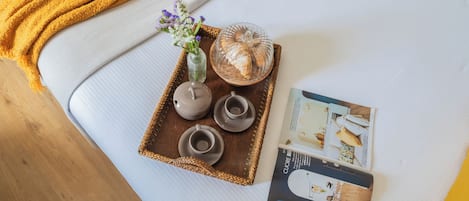 Ein ordentlich gedeckter Tablett mit einem Keramik-Teeservice, einer Glaskaraffe und einer Blumenvase auf einem weißen Sofa.