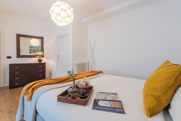 Een verzorgde slaapkamer met een bed, een nachtkastje met lamp, een dressoir en een lijst met een afbeelding aan de muur.