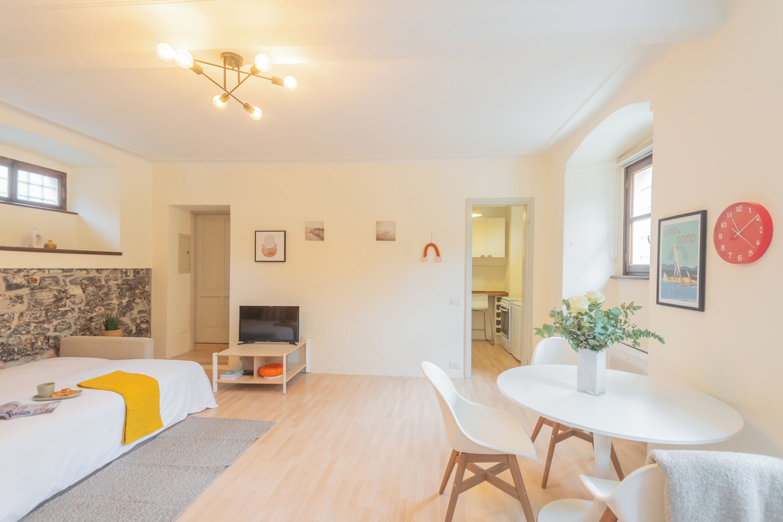 A modern living room with a sofa, a TV, a dining table with chairs, and a kitchen in the background.