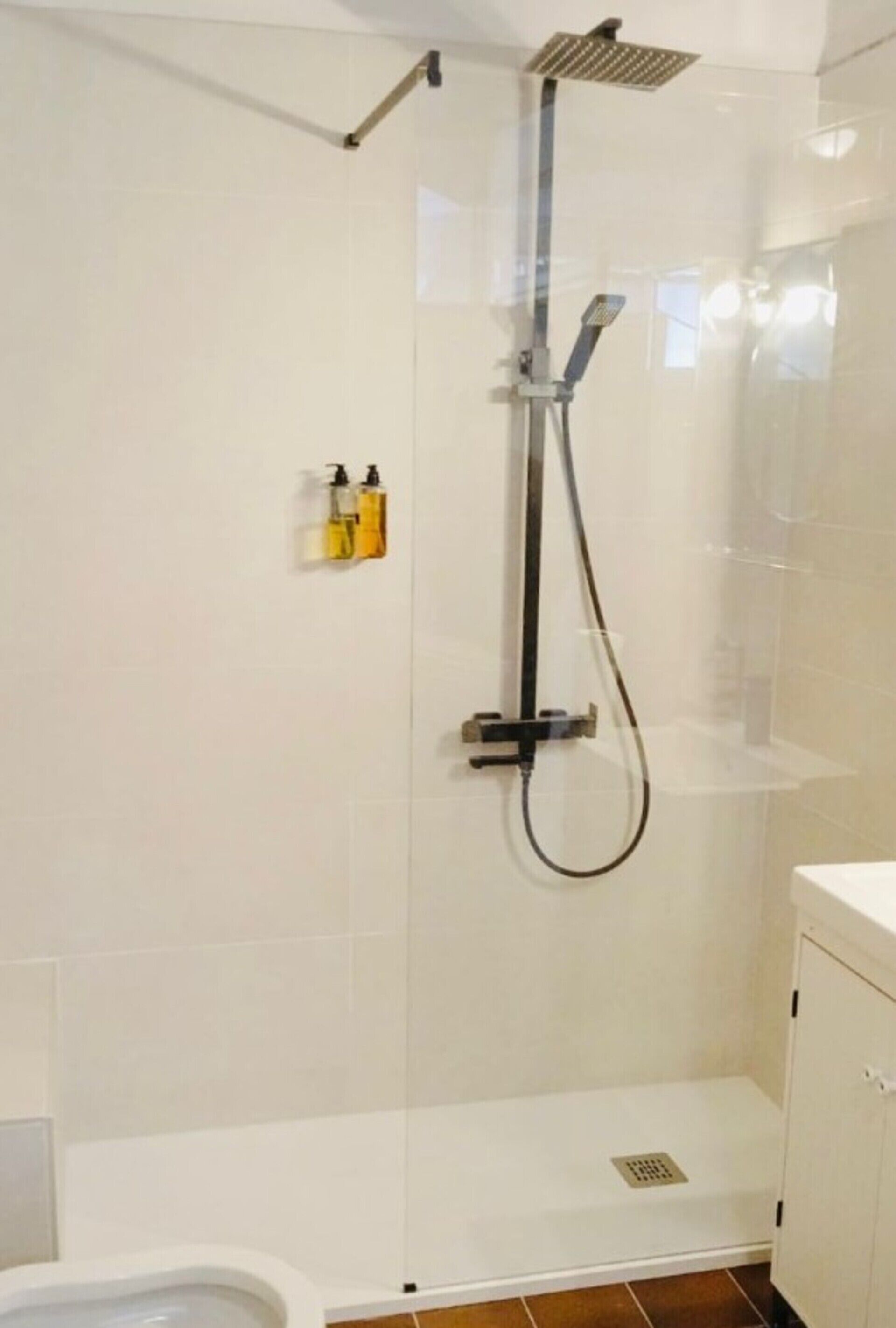 Un cerramiento de ducha con un cabezal de ducha de mano y un grifo empotrado en la pared.