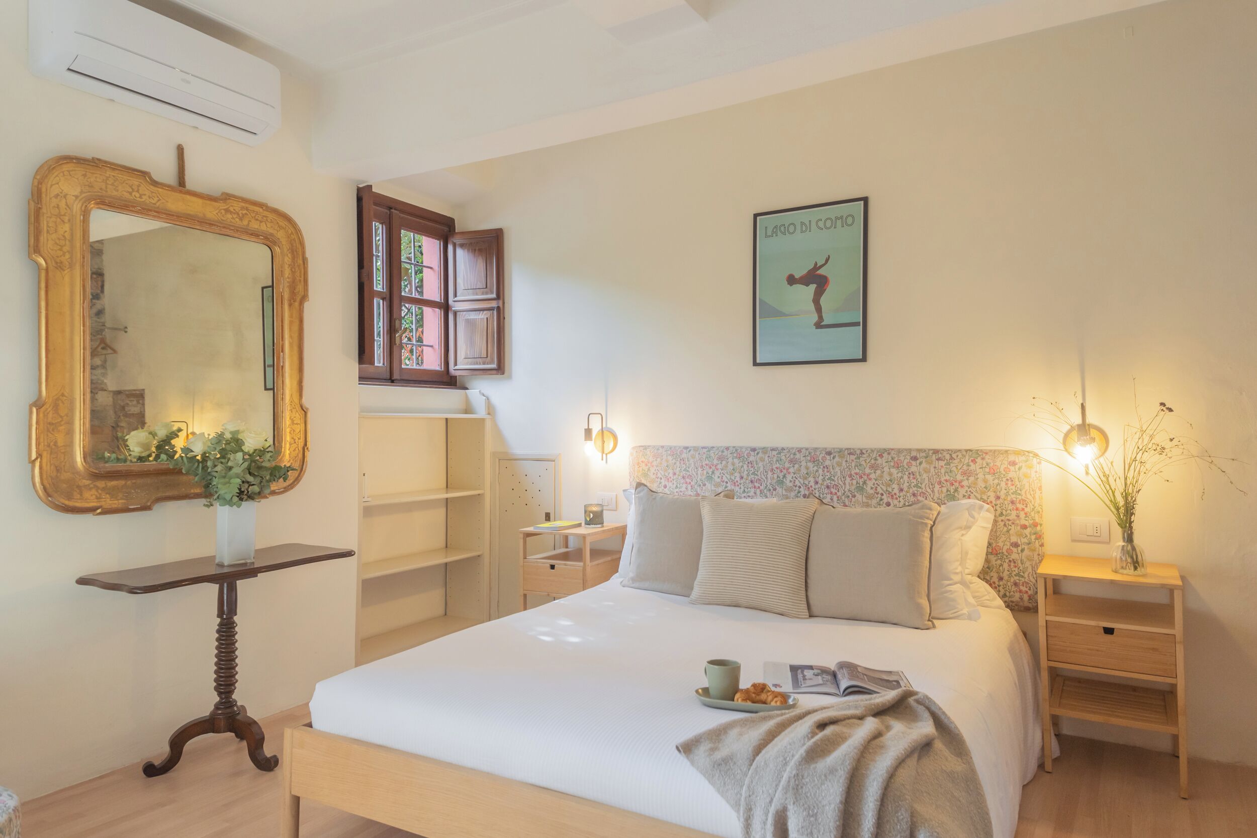 A neatly arranged bedroom with a large bed, bedside tables, a mirror, and a framed picture on the wall.