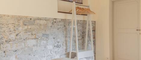 A room with a stone wall, a bed with a pillow and a cup, a wooden hanger, and a door.