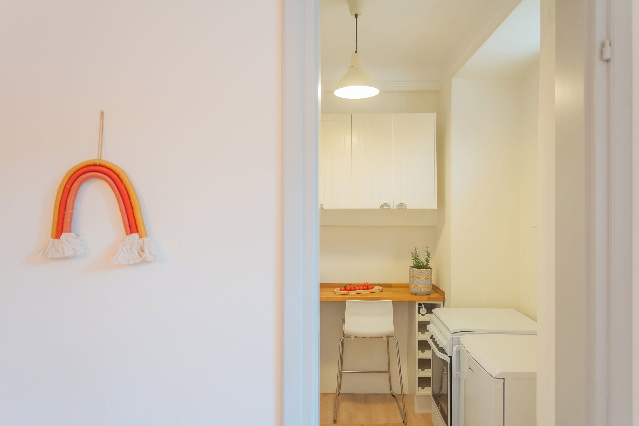A kitchen with white cabinets, a wooden countertop, a white chair, and a white refrigerator.
