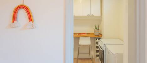 A kitchen with white cabinets, a wooden countertop, a white chair, and a white refrigerator.