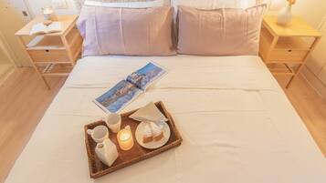 Una cama bien hecha con una bandeja de desayuno, un libro y una vela sobre una mesita de noche.