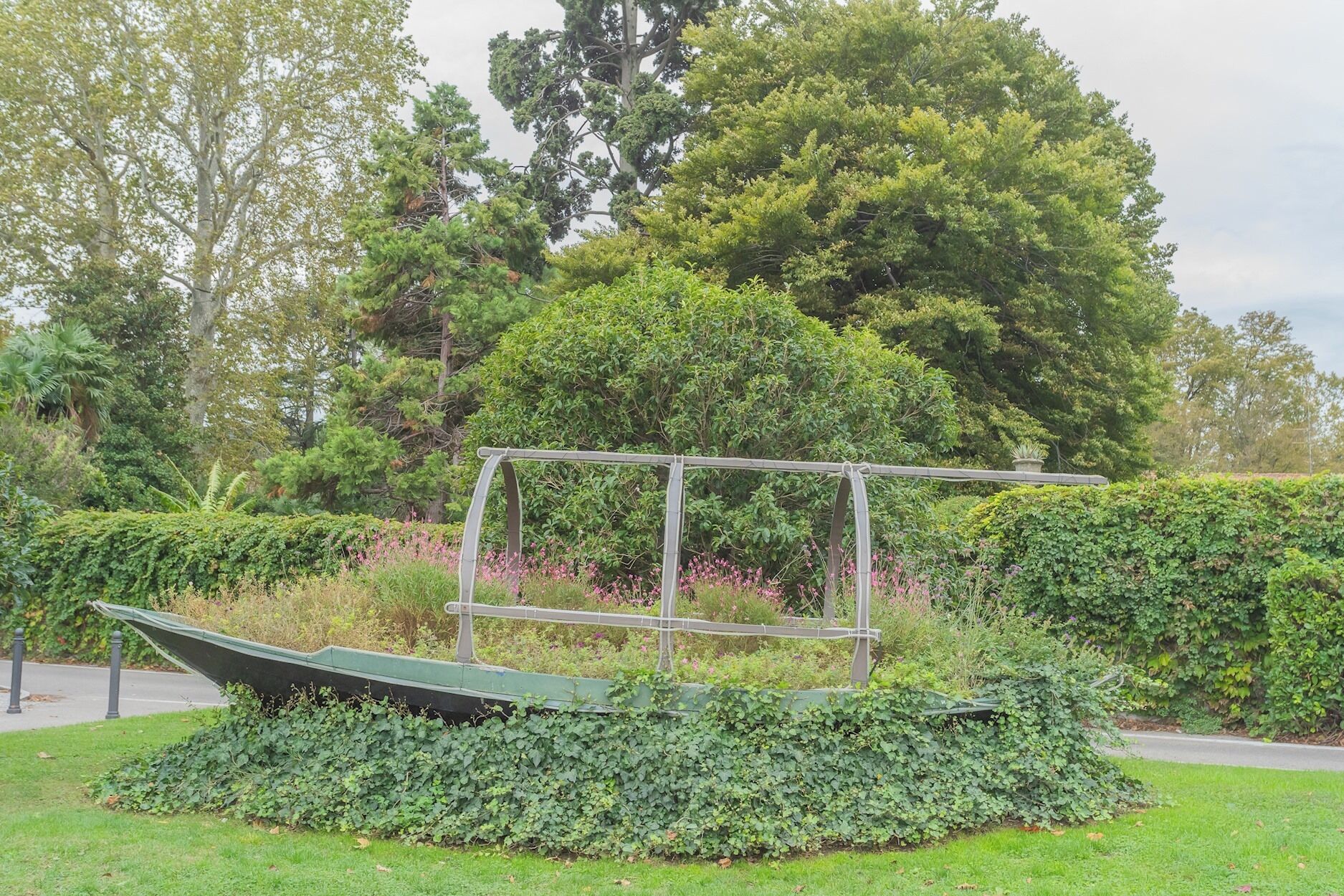 A garden with a metal structure resembling a boat, surrounded by lush greenery and trees.