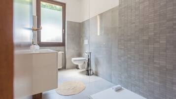 A modern bathroom with a glass shower enclosure, a white bathtub, and a toilet.