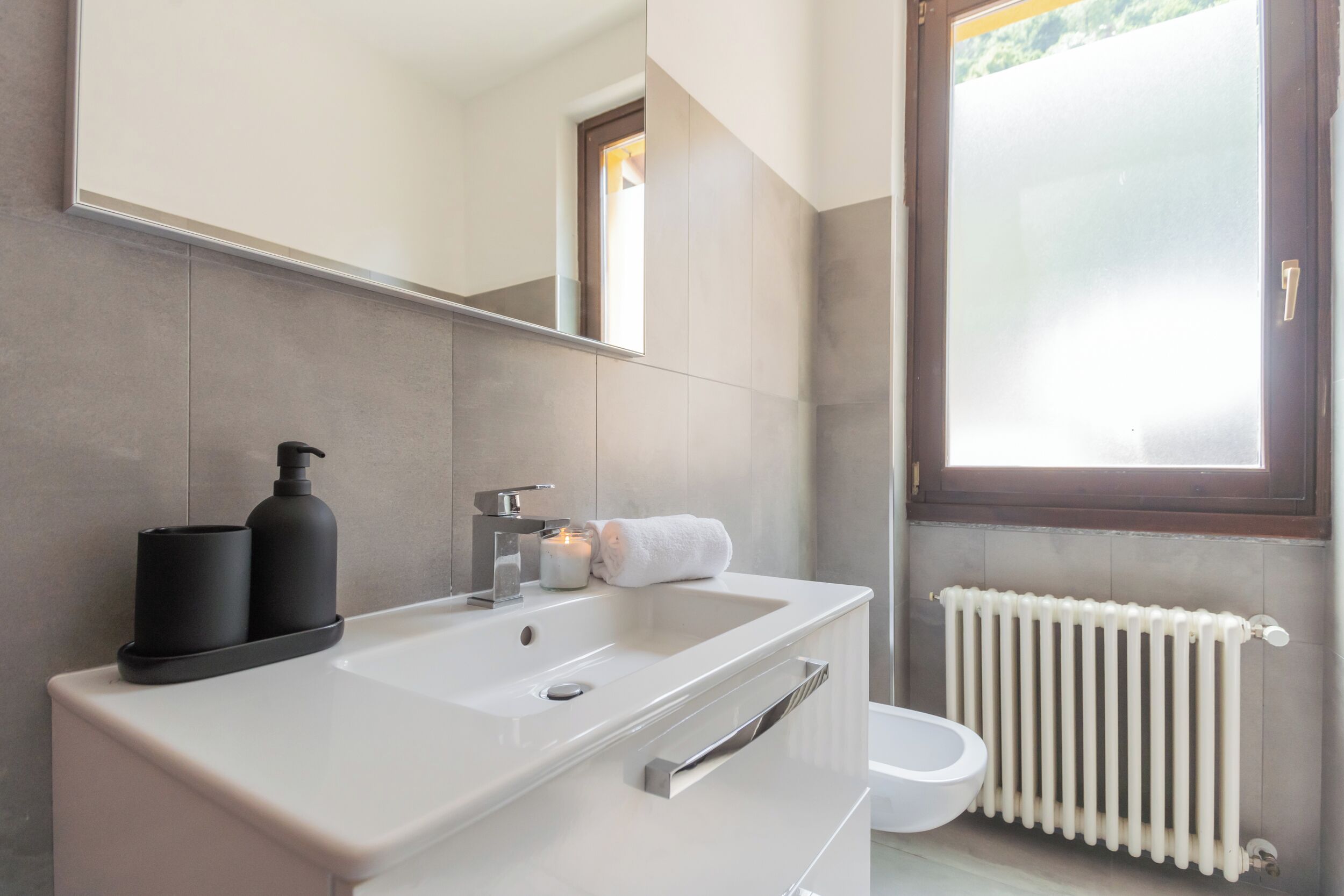 Un baño moderno con un lavamanos blanco, un espejo, una toalla y una ventana con vistas.