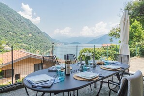 A table set outdoors with a view of a lake and mountains, surrounded by a fence. - Harmony on the Lake by Rent all Como (Argegno)