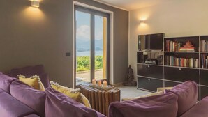 A living room with a purple sofa, a wooden side table with candles, a bookshelf, and a view of a vineyard through a sliding door. - Harmony on the Lake by Rent all Como (Argegno)