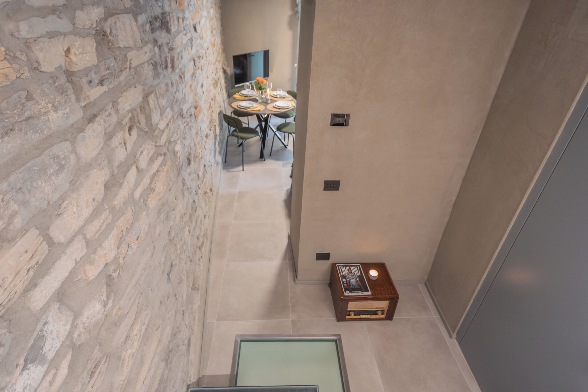 A modern interior with a stone wall, a dining area with a round table and chairs, and a small wooden side table with a magazine.