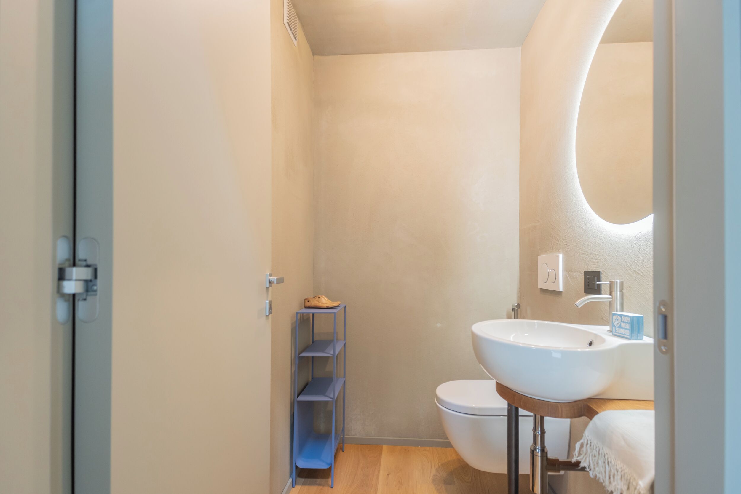 A modern bathroom with a white sink, toilet, and a blue shelving unit.