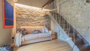 A modern living room with a stone wall, a wooden staircase, and a beige sofa with colorful cushions. - Urio's Castle Suites by Rent all Como (Carate Urio)