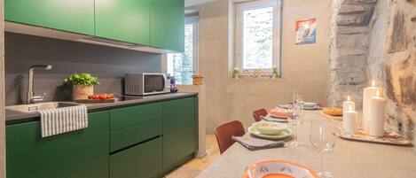 A modern kitchen with green cabinets, a microwave, and a dining area with a table set for two, candles, and a window with a view of trees.