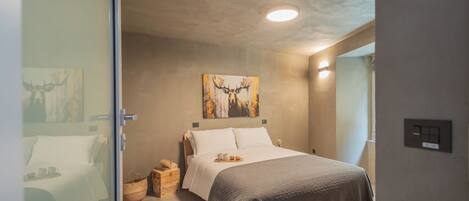 A modern bedroom with a large bed, a painting of a deer, a bedside table with a lamp, and a window with curtains.