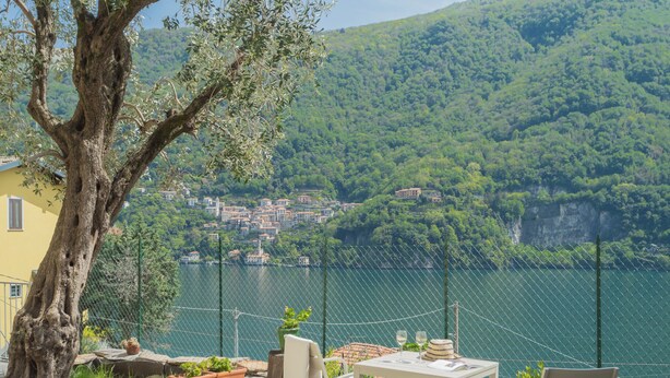 A terrace with a table and chairs overlooking a lake, surrounded by potted plants and a tree. - La Quiete With Private Garden by Rent all Como (Laglio)