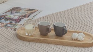 A neatly made bed with white bedding and decorative pillows, a wooden tray with a glass of milk, two mugs, and meringue cookies on a textured white surface. - La Quiete With Private Garden by Rent all Como (Laglio)