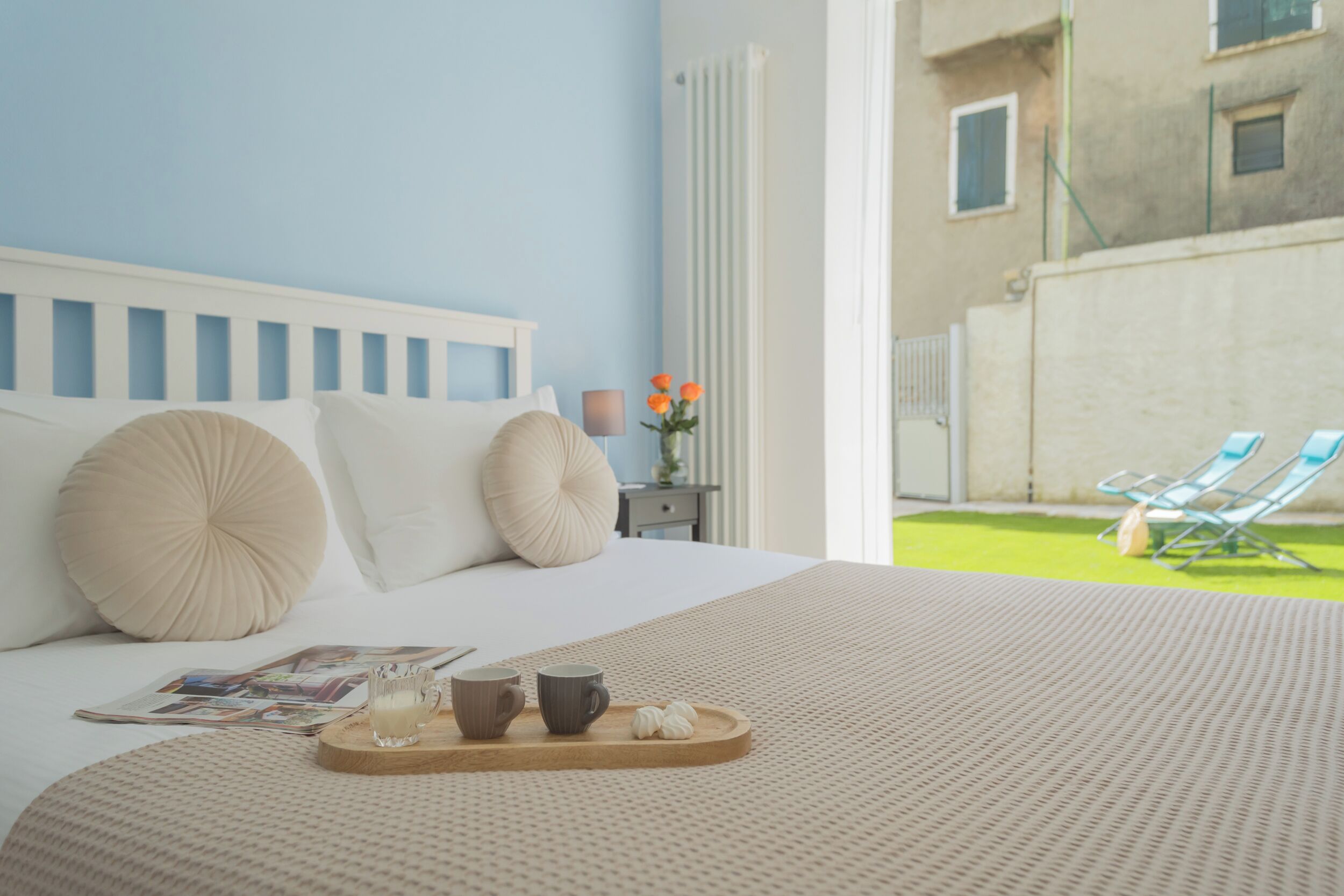 A neatly made bed with a tray of breakfast items, a magazine, and a vase of flowers on a nightstand.