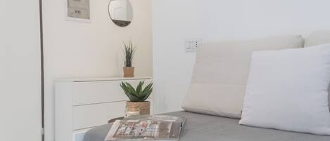 A modern bedroom with a bed, a bedside table with a plant, a mirror, and a wall-mounted control panel.