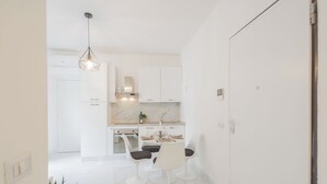 A modern kitchen with white cabinetry, a marble countertop, and a dining area with white chairs. - Luce Apartment by Rent all Como (Como)
