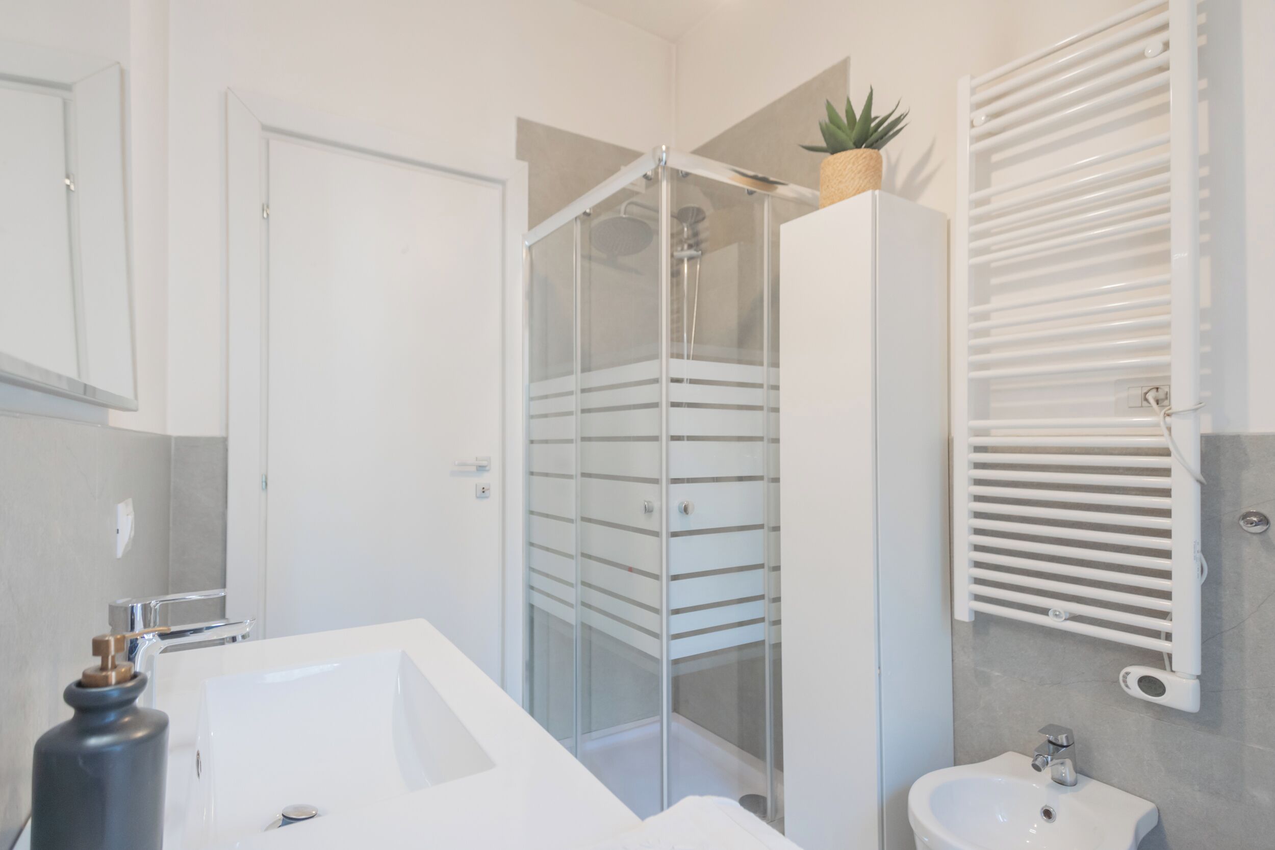A modern bathroom with a glass shower enclosure, a white sink, and a towel rack.