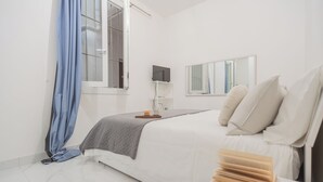 A bedroom with a bed, a bedside table with a candle, a TV, and a mirror. - Luce Apartment by Rent all Como (Como)