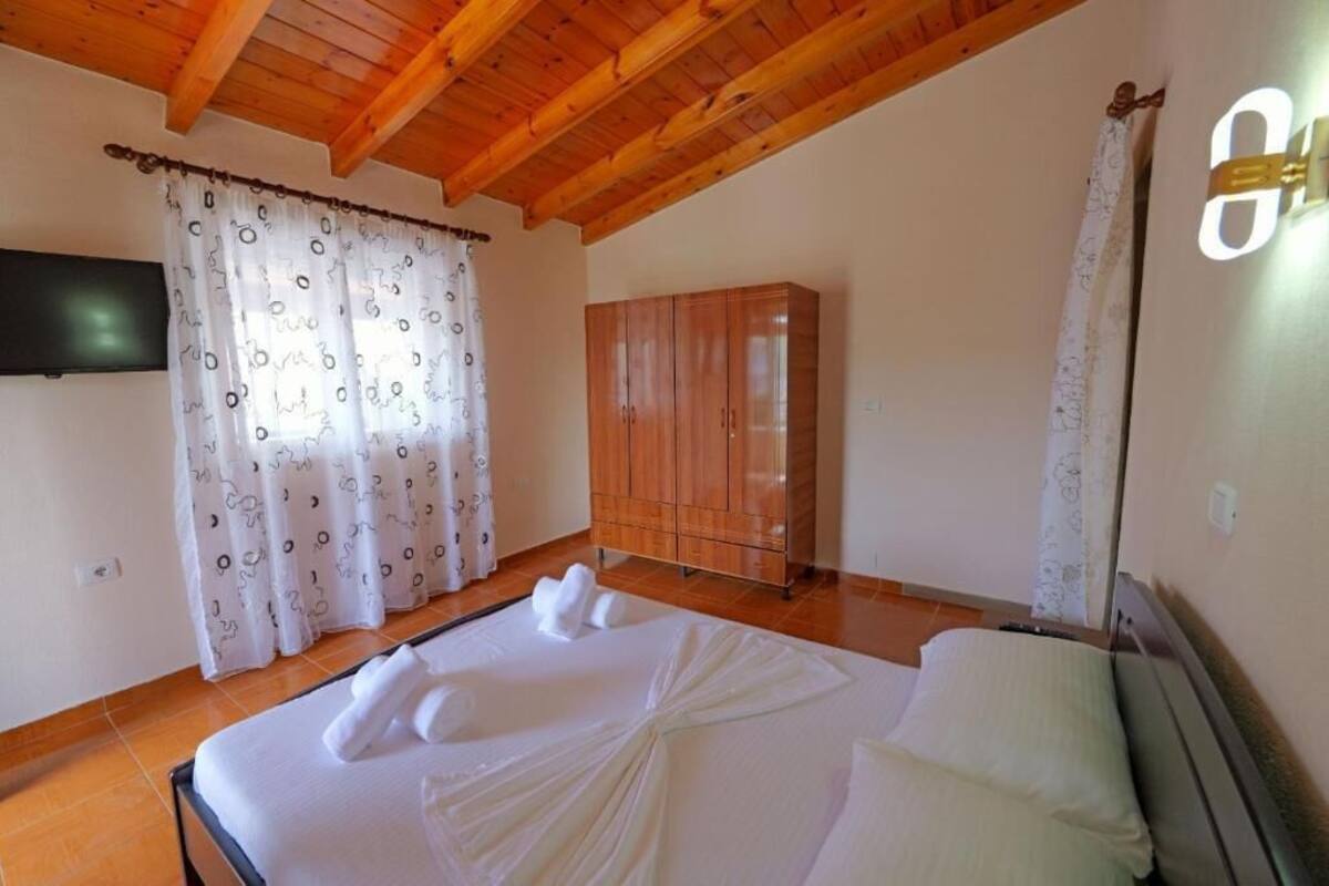 A bedroom with a wooden ceiling, a bed with white linens, a wardrobe, and a TV on the wall.