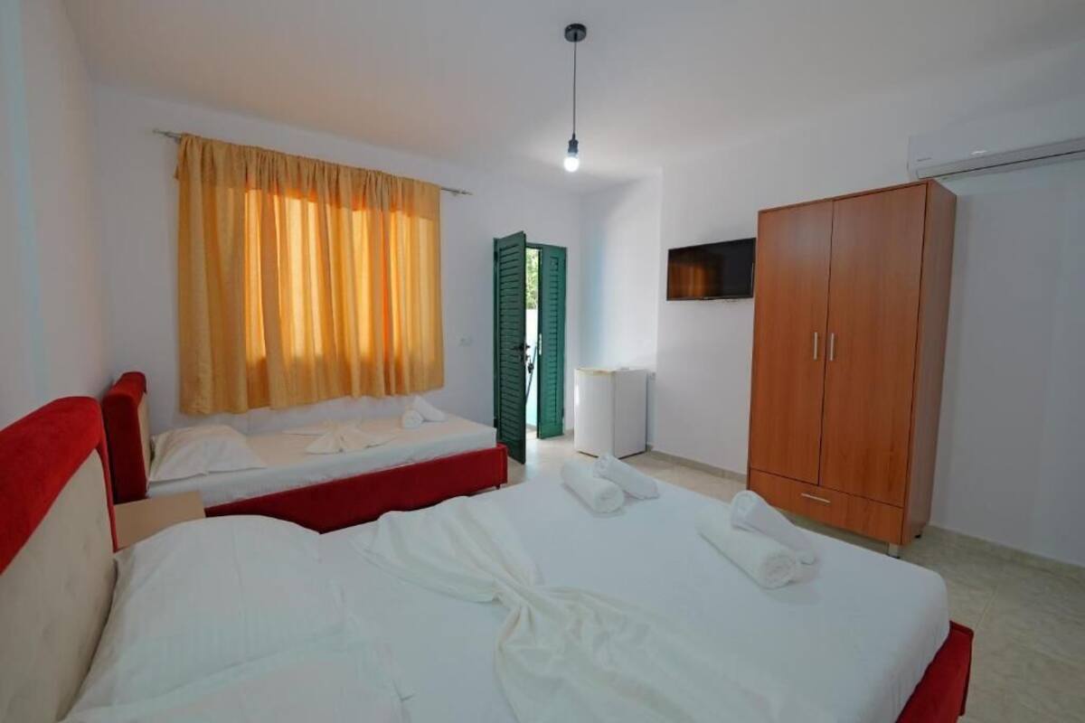 A hotel room with two single beds, a wardrobe, a television, and a window with curtains.