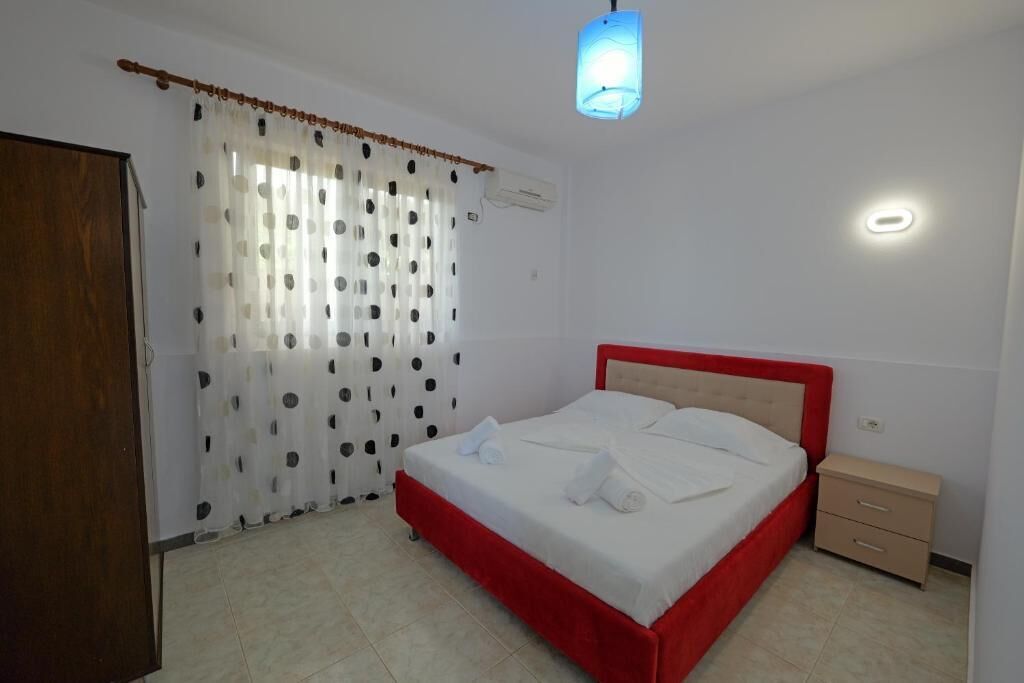 Ein Schlafzimmer mit Bett, Nachttisch, Holztür und einem Fenster mit Vorhängen.