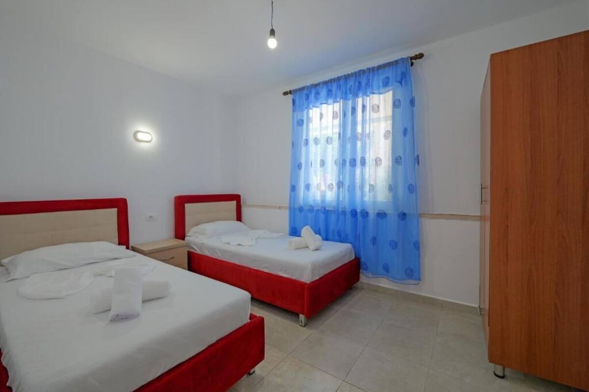 A hotel room with two beds, a wardrobe, and a window with blue curtains.