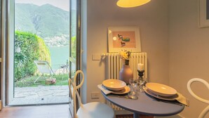 Un comedor con una mesa dispuesta para dos personas, vista a un paisaje montañoso a través de un ventanal, y un cuadro en la pared.