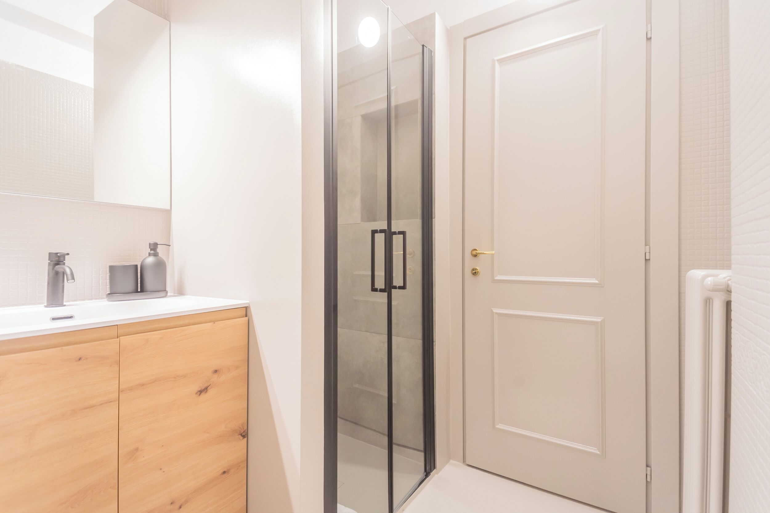 A modern bathroom with a glass shower enclosure, a wooden vanity, and a white door.