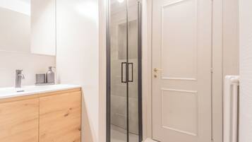 A modern bathroom with a glass shower enclosure, a wooden vanity, and a white door.