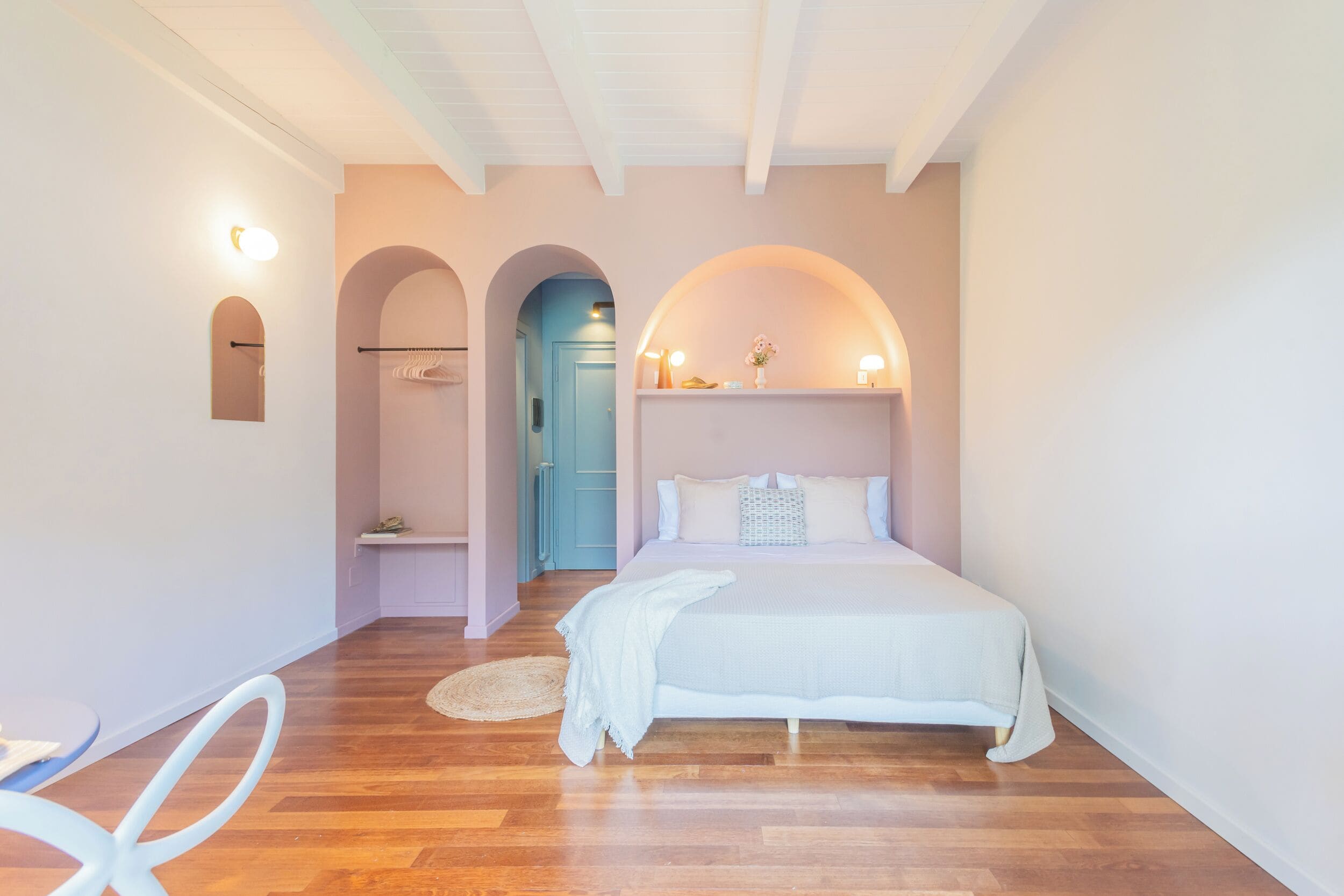A bedroom with a large bed, wooden flooring, a small seating area, and a bathroom with a blue door.