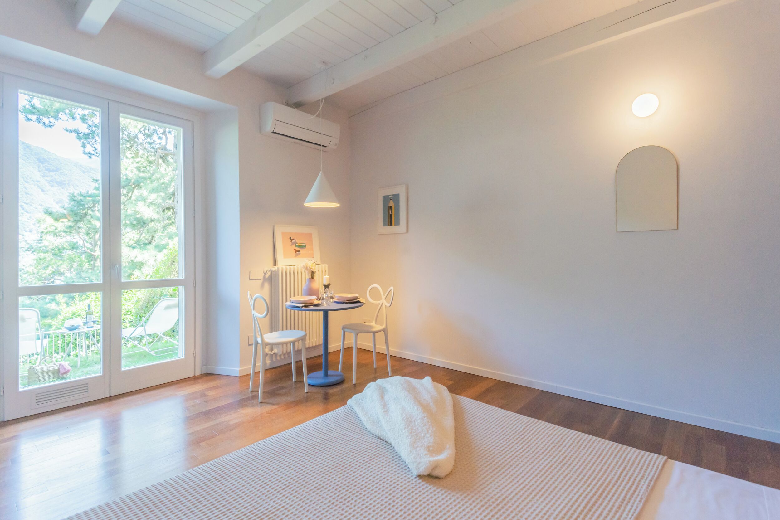 A bright room with a large window, a round table with chairs, and a white rug.