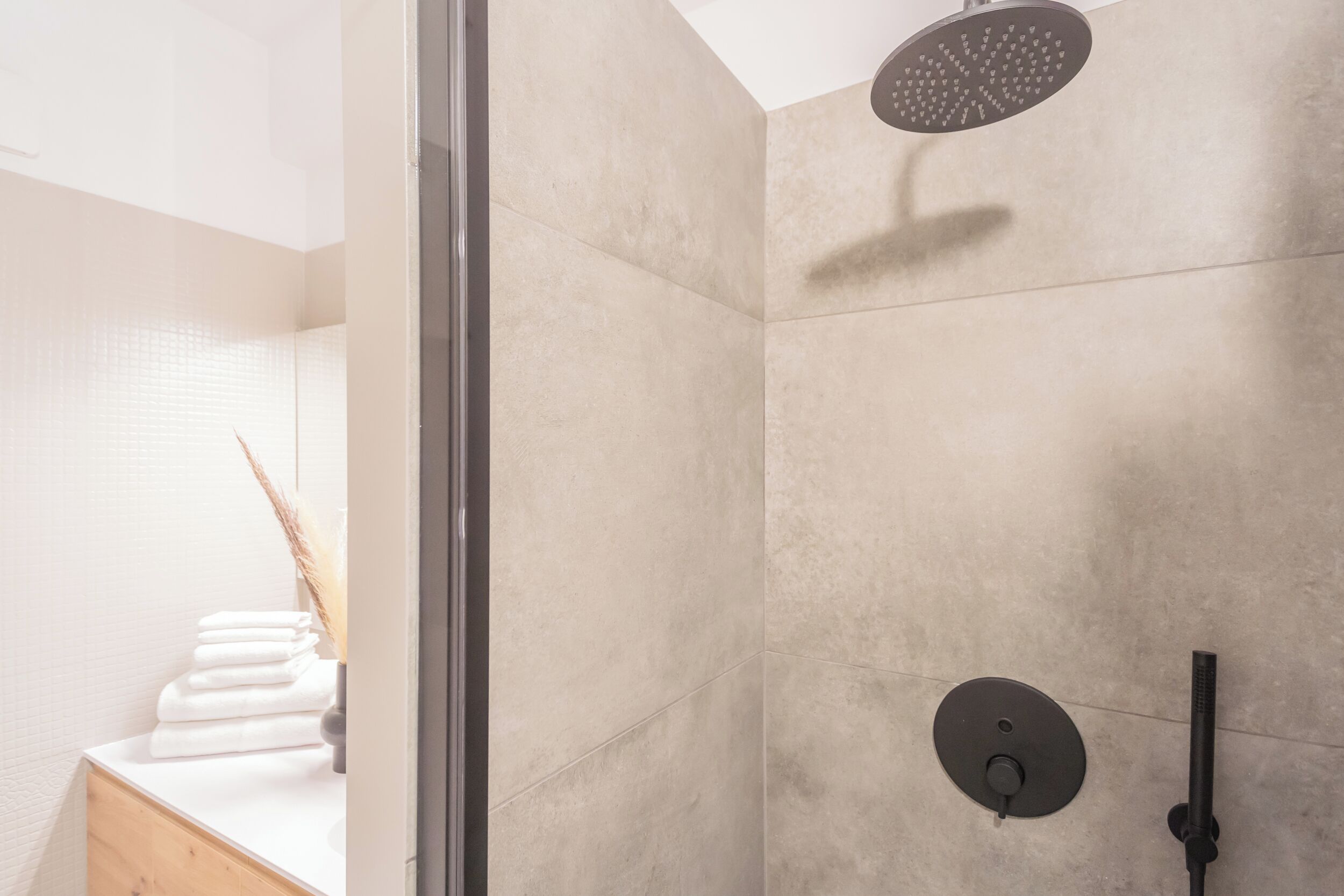 Une salle de bain moderne dotée d’une douche à parois de verre, d’un plan de toilette blanc sur lequel sont pliées des serviettes, et d’un design minimaliste.