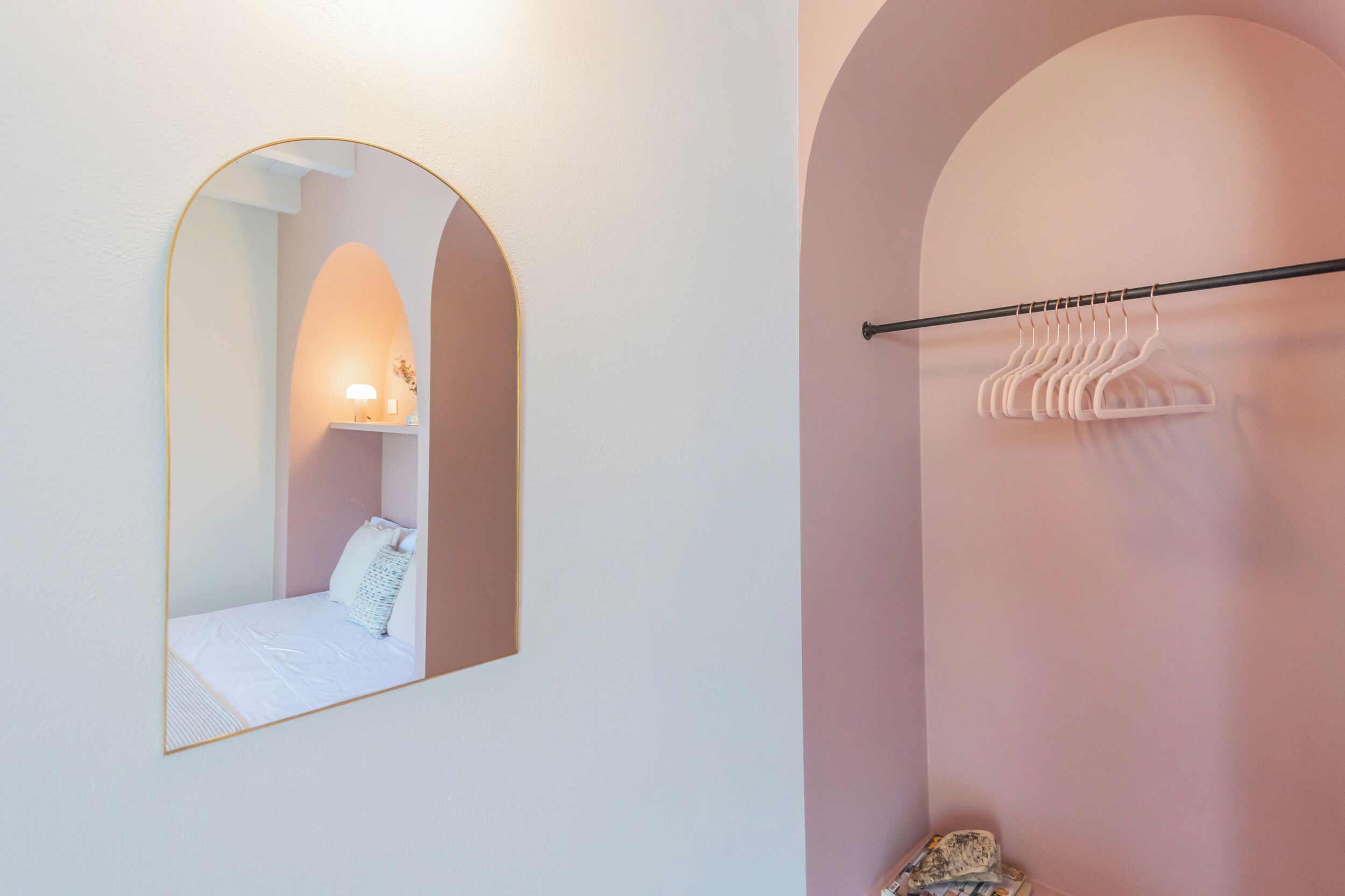 A bedroom with a bed, a mirror, a wall-mounted light, and a clothing rack.