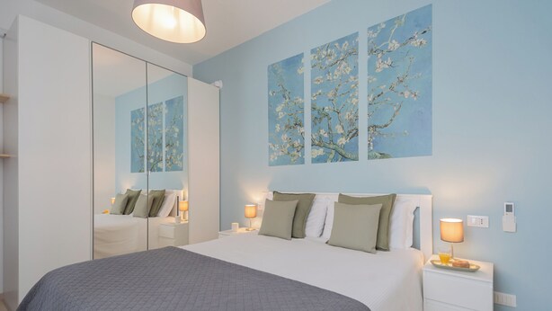 Un dormitorio con cama, mesitas de noche, tocador, espejo y decoración en la pared.