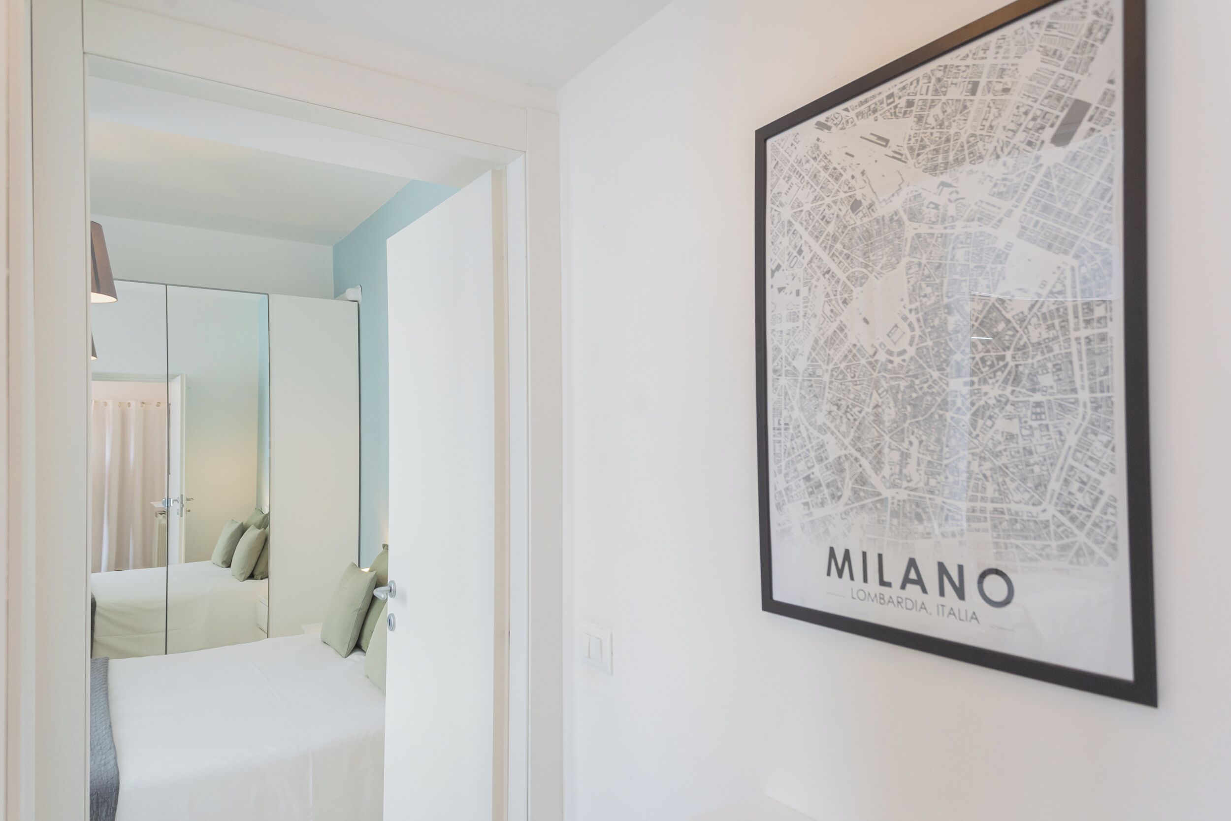 A hotel room with a bed, a mirror, and a framed map of Milan on the wall.