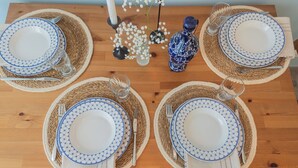 Una mesa de comedor dispuesta con cuatro platos, cada uno con un diseño azul y blanco, y un florero azul con motivos de mosaico.