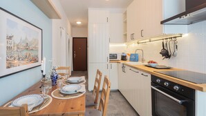 Una cocina compacta con armarios blancos, una encimera de madera y un horno empotrado. Hay una mesa de comedor preparada con platos y vasos.